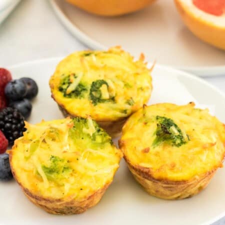 three broccoli cheese egg muffins on a plate next to a small plate with a grapefruit cut in half