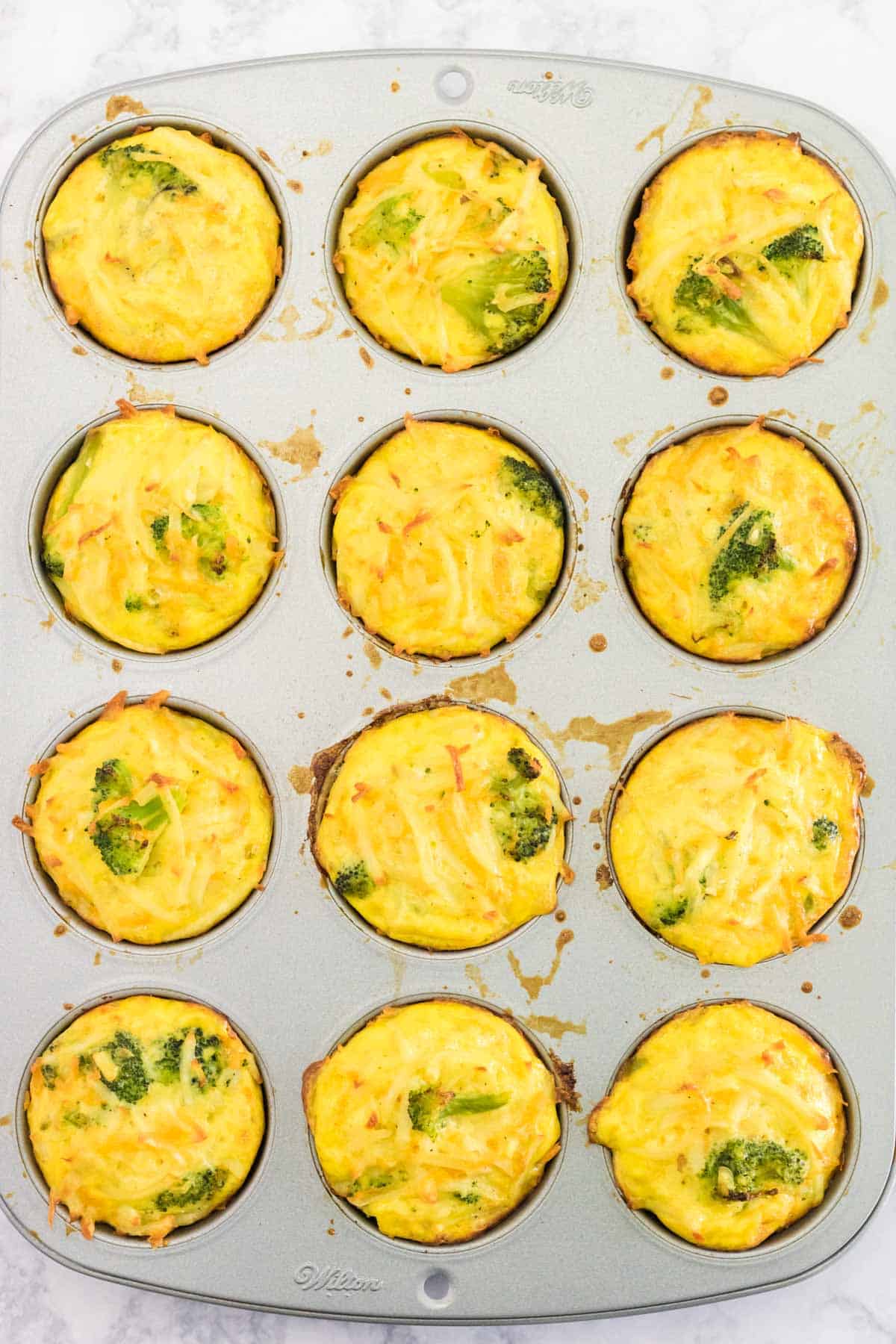 a muffin pan with 12 baked broccoli cheese egg muffins