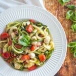 zoodles caprese salad in a serving bowl on a wooden tabletop next to a red plaid napkin