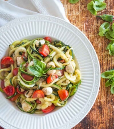 zoodles caprese salad in a serving bowl on a wooden tabletop next to a red plaid napkin
