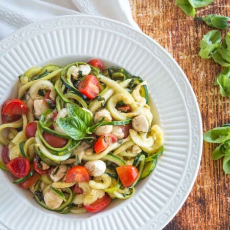 zoodles caprese salad in a serving bowl on a wooden tabletop next to a red plaid napkin