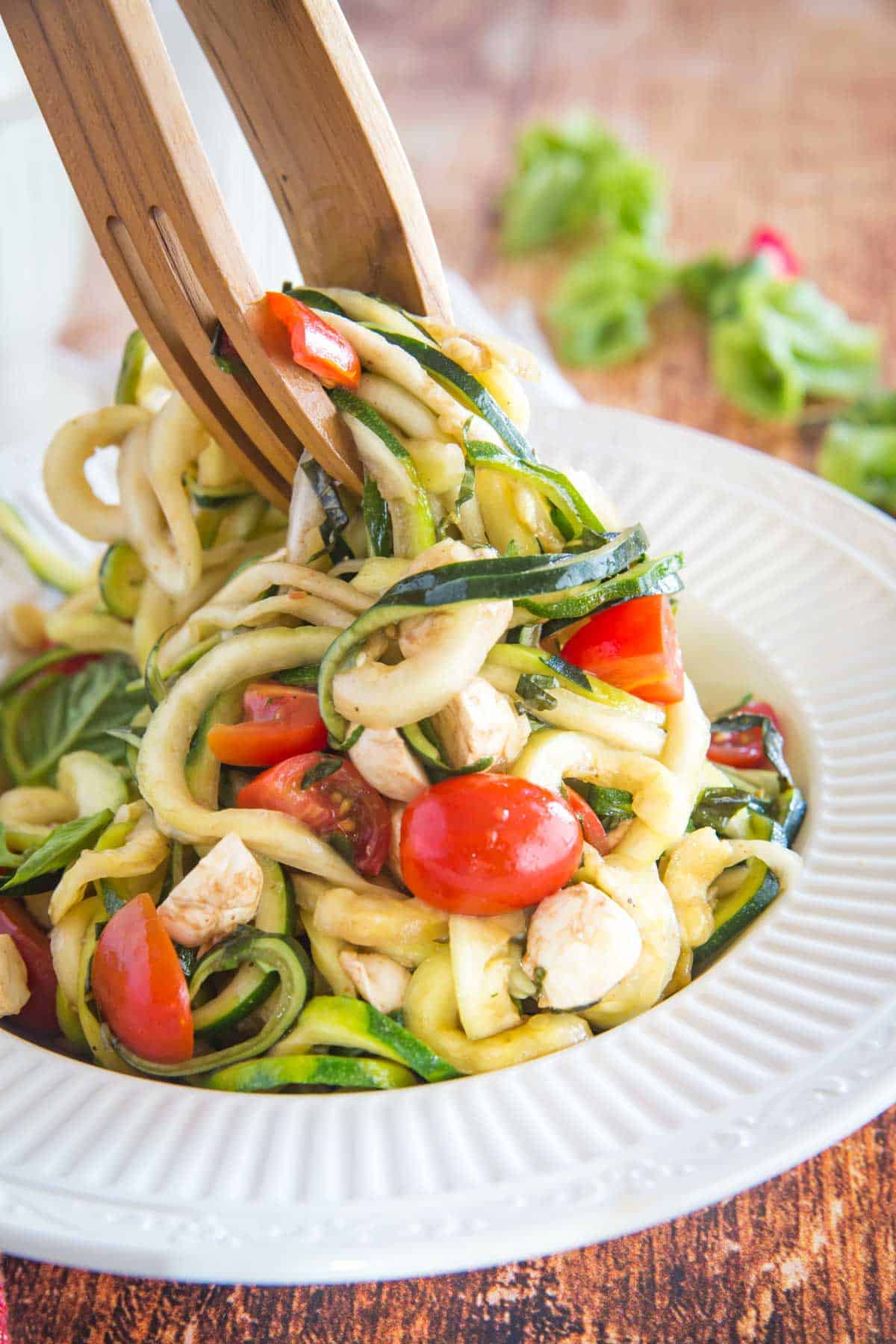 using tongs to toss zucchini noodles, tomatoes, and fresh mozzarella