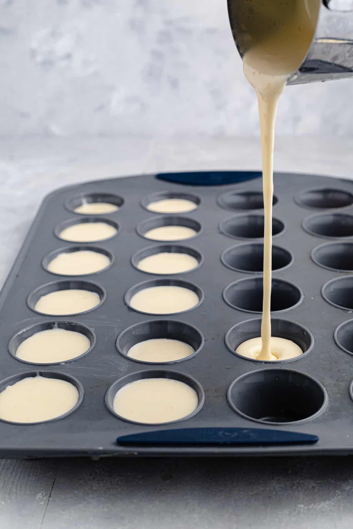 pouring cheese bread batter into a mini muffin tin