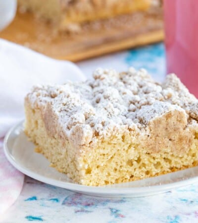 one piece of gluten free crumb cake on a plate with a fork and a pink coffee mug