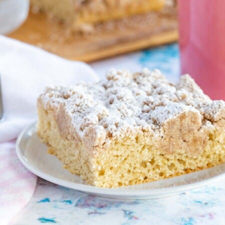 one piece of gluten free crumb cake on a plate with a fork and a pink coffee mug