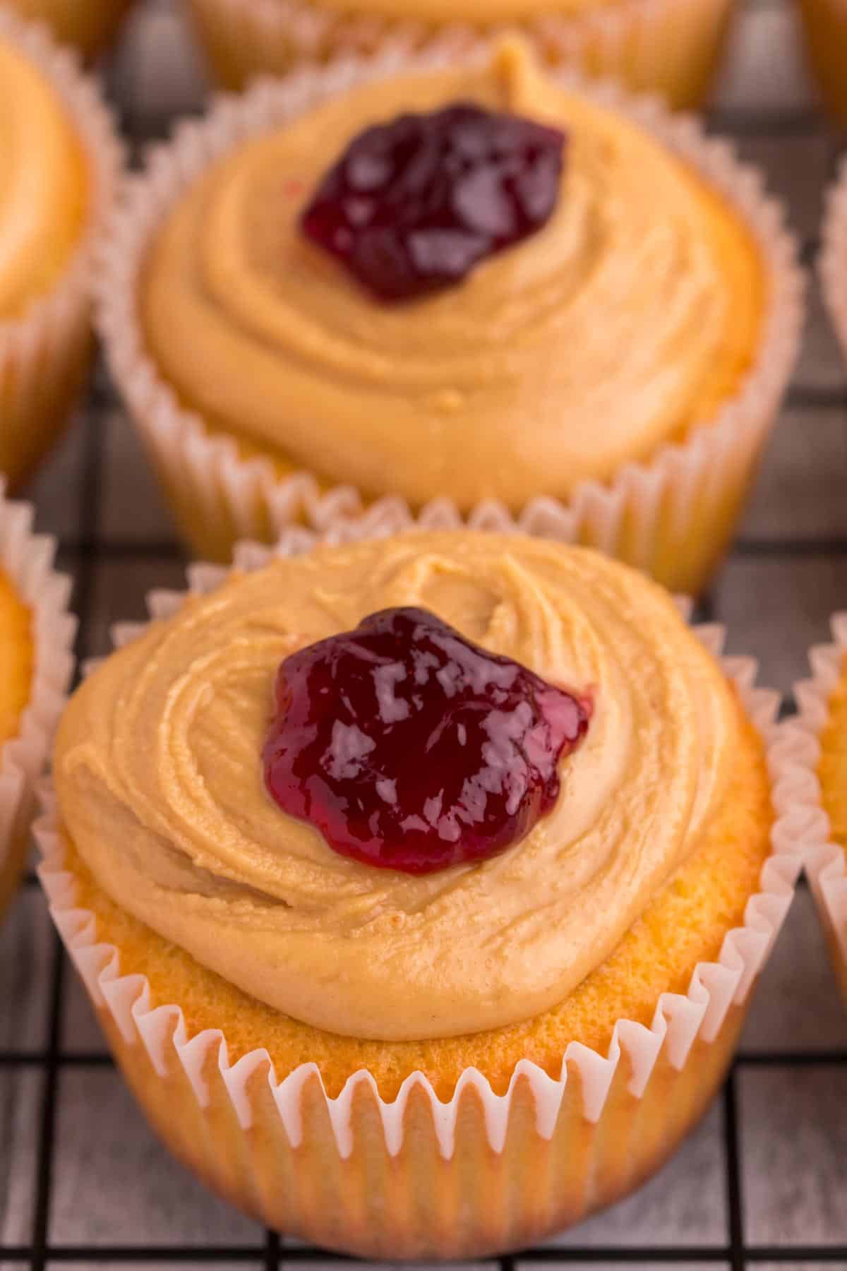 gluten free peanut butter and jelly cupcakes on a cooling rack topped with peanut butter frosting and a dollop of jelly