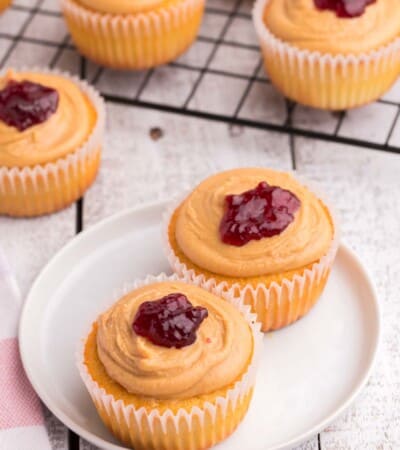 two cupcakes topped with peanut butter frosting and a dollop of jelly on a small white plate