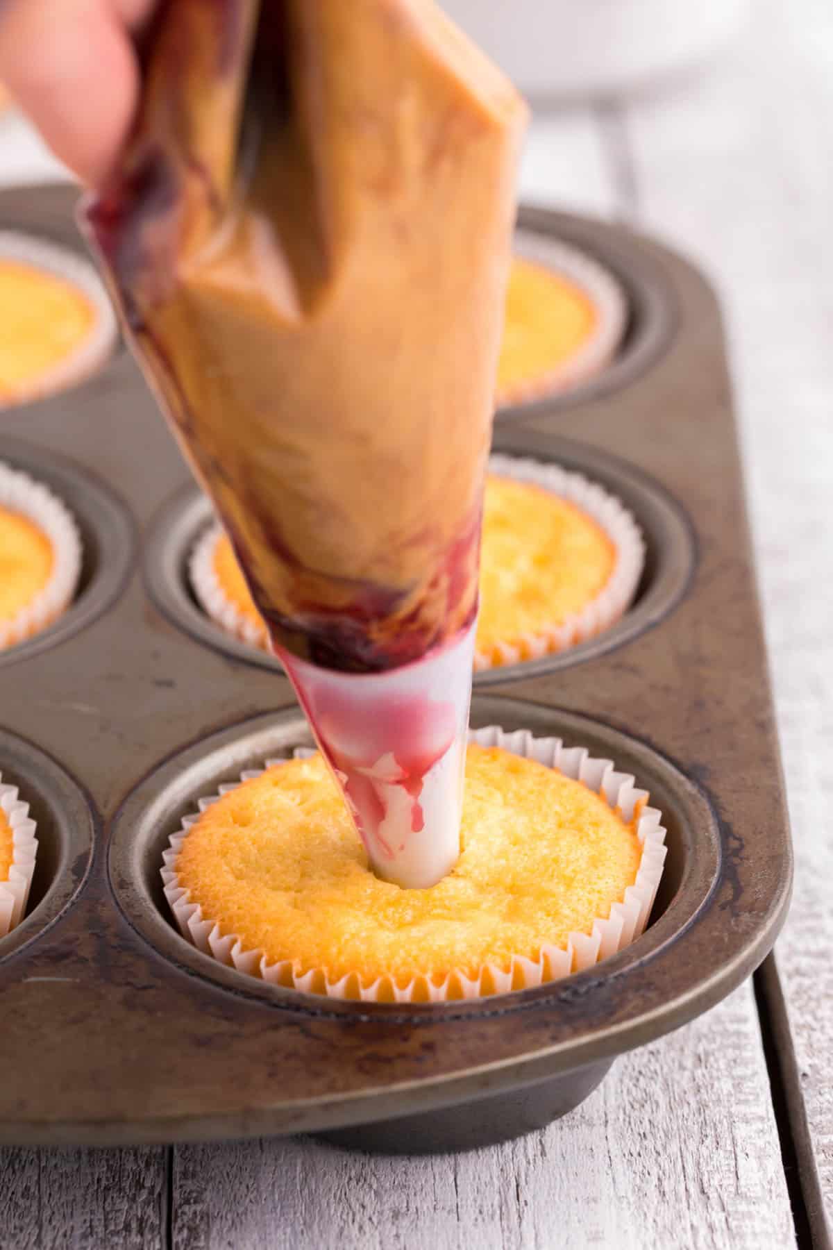 a piping bag filled with peanut butter and jelly inserted into the top of a vanilla cupcake