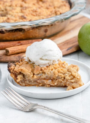 close up on a slice of dutch apple pie with ice cream and cinnamon sticks