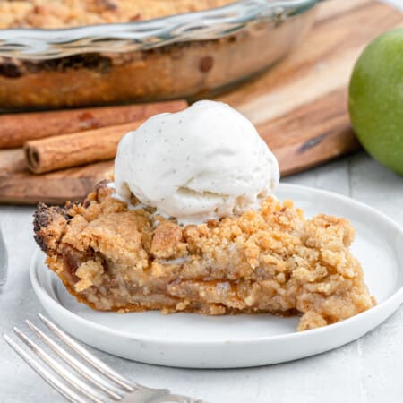 close up on a slice of dutch apple pie with ice cream and cinnamon sticks