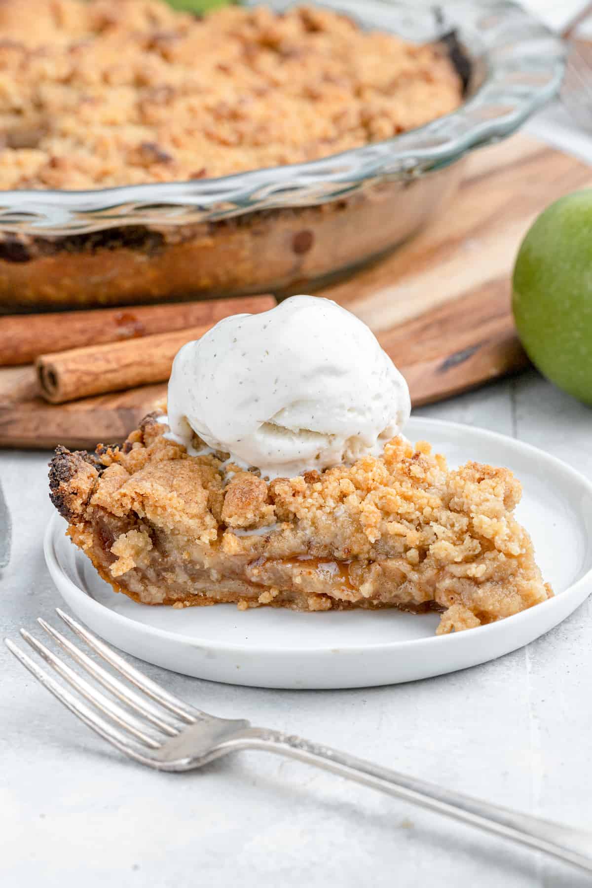 close up on a slice of dutch apple pie with ice cream and cinnamon sticks