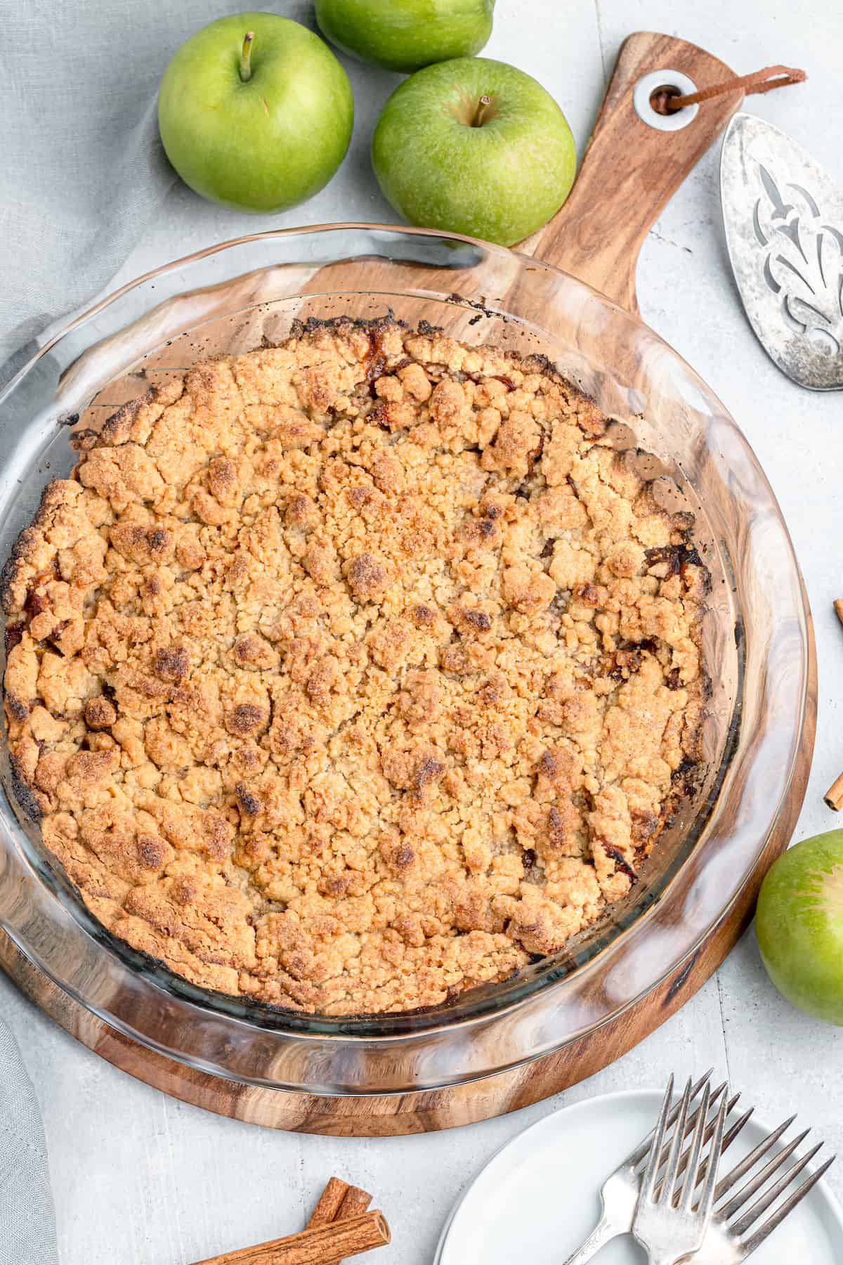 whole apple pie with crumb topping with raw granny smith apples on the side