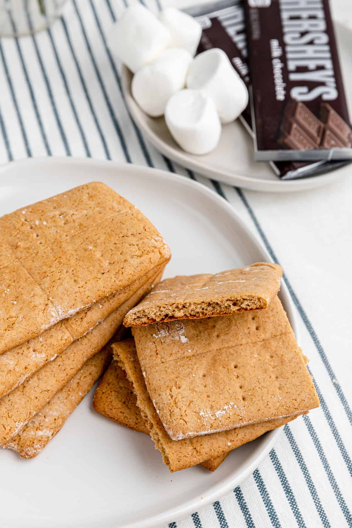 white plate with stacks of graham crackers with marshmallows and chocolate in the background