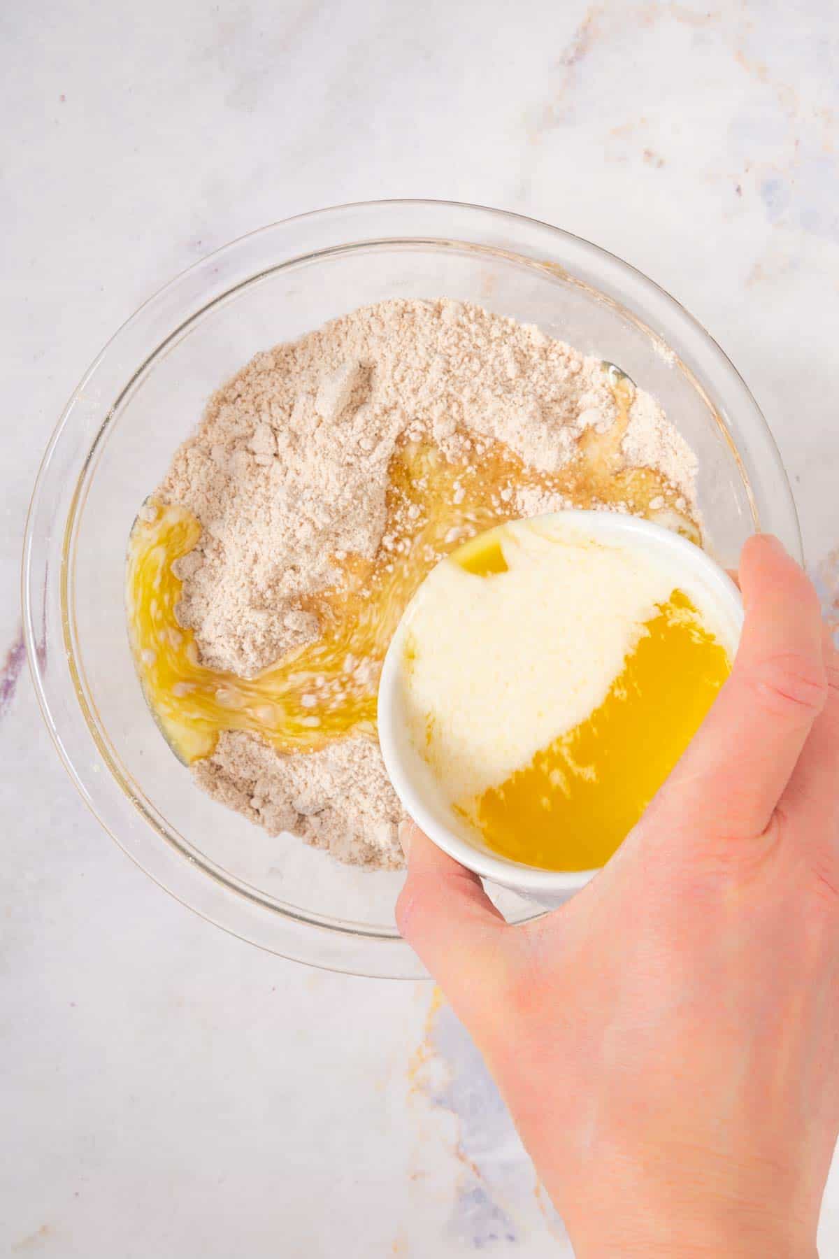 pouring melted butter into a mixing bowl with flour and cinnamon