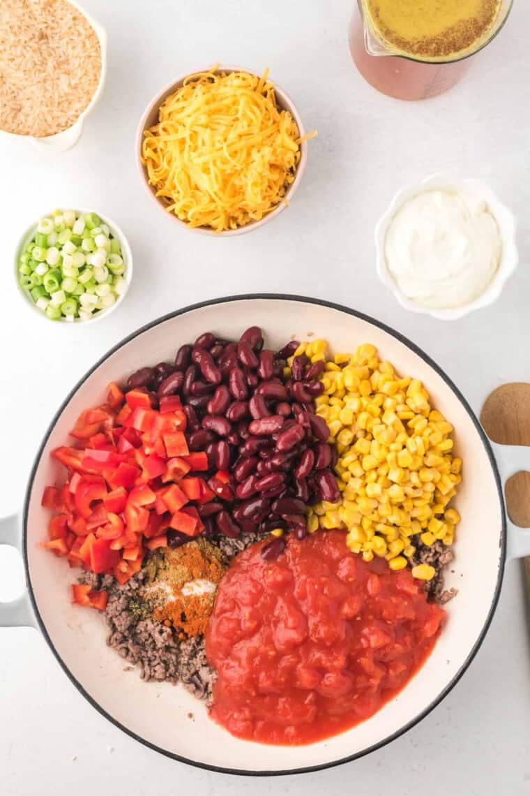 cooked ground beef in a skillet with the canned diced tomatoes, corn, kidney beans, chopped red bell pepper, and spices added on top