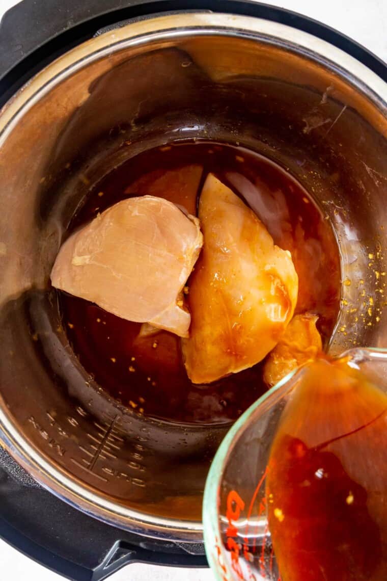 pouring sauce mixture over raw chicken breasts in the instant pot