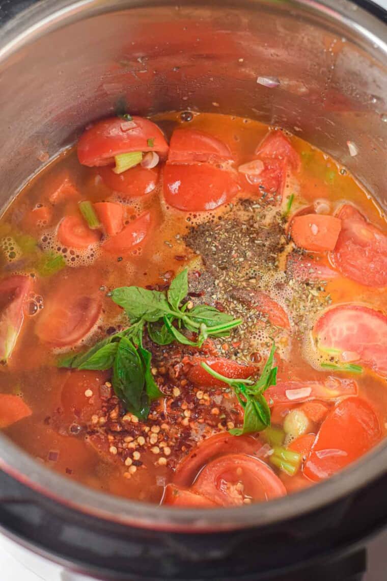 Sauteed vegetables in vegetable stock with basil, red pepper flakes, salt, pepper, and dried oregano inside the instant pot.