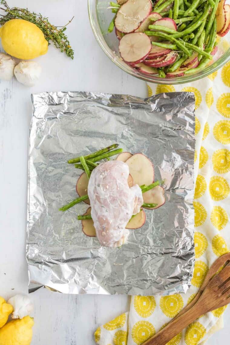 marinated raw chicken breasts on top of the green beans and potatoes on the piece of aluminum foil