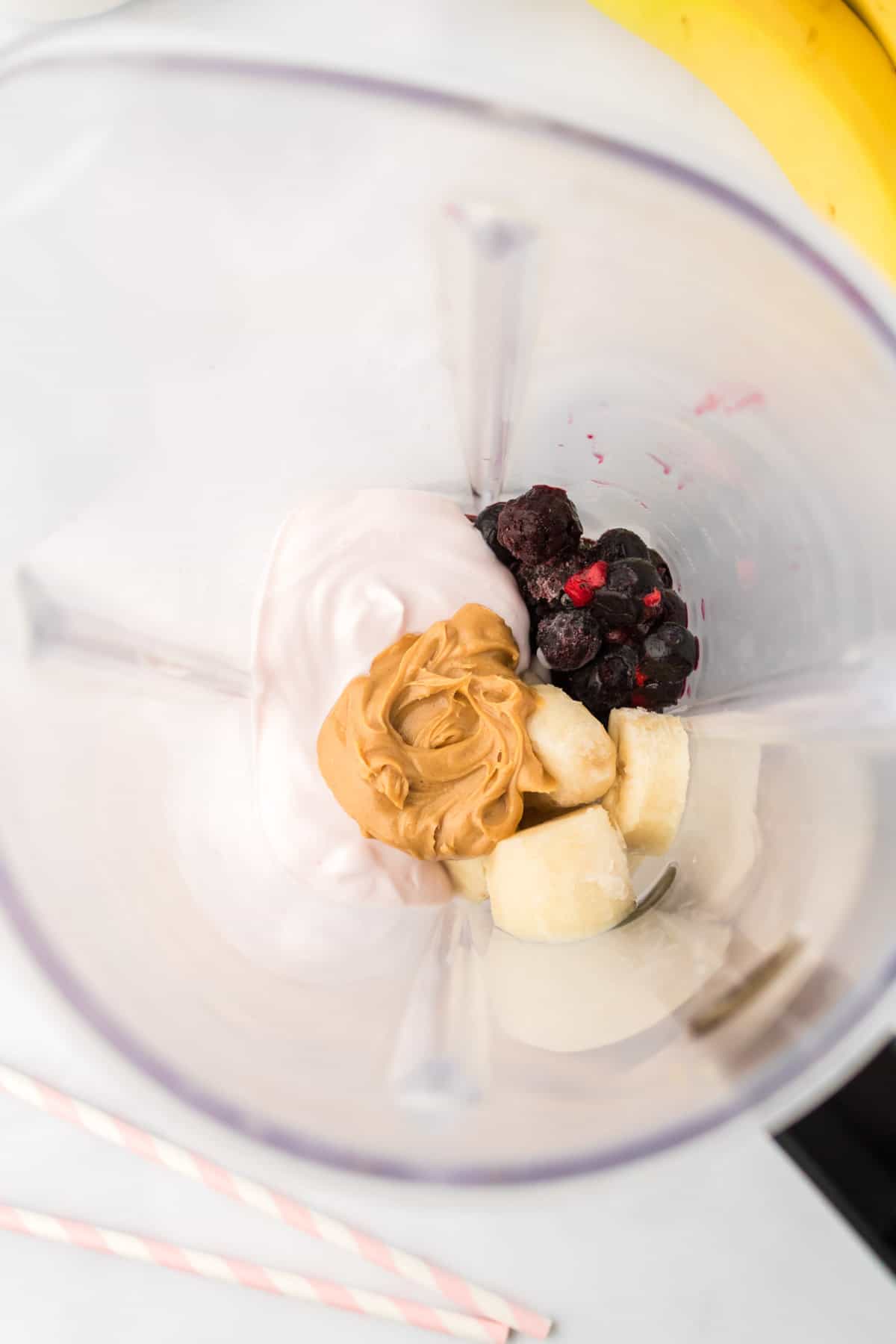 Frozen berries and bananas, yogurt, and peanut butter in a blender jar.