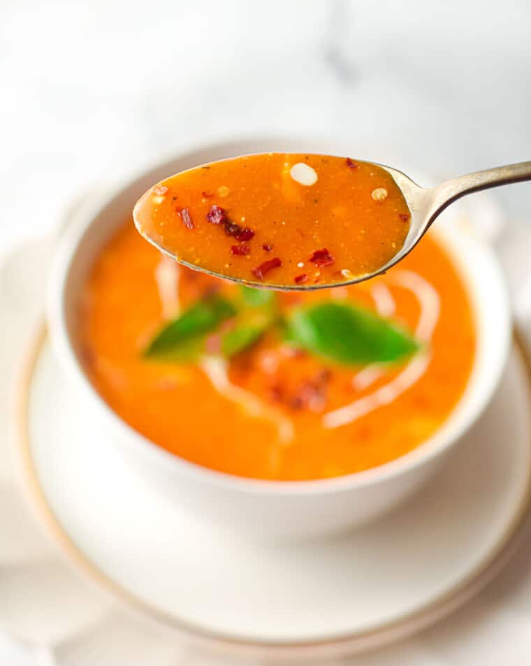 a soup spoon with tomato soup held above a bowl