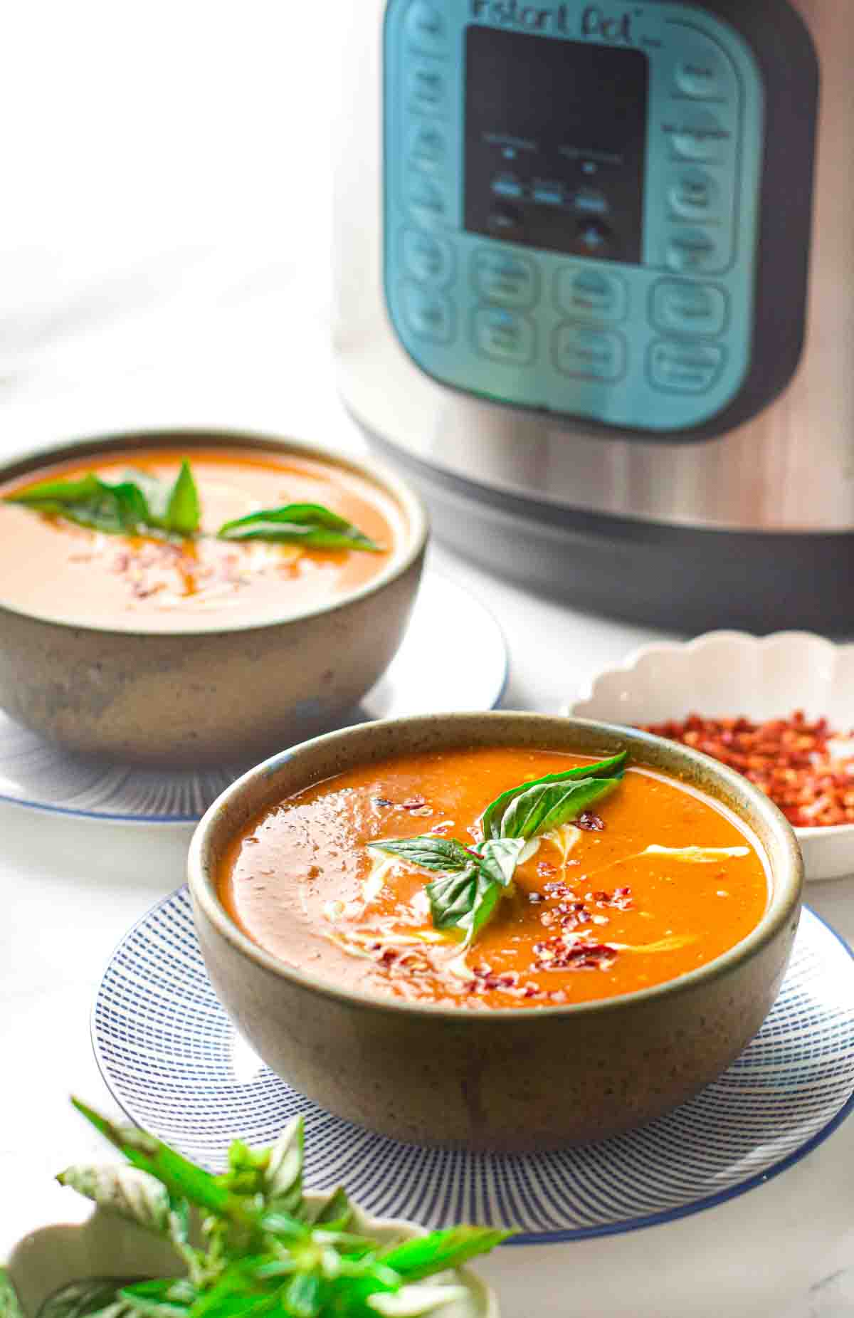 Two bowls of creamy tomato soup on saucers in front of an instant pot.