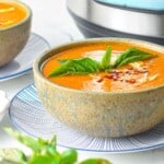 bowl of creamy tomato soup garnished with basil on top of a sauce next to an instant pot