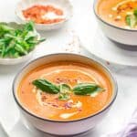 A bowl of creamy tomato soup garnished with basil leaves with text overlay that says "Instant Pot Tomato Basil Soup".