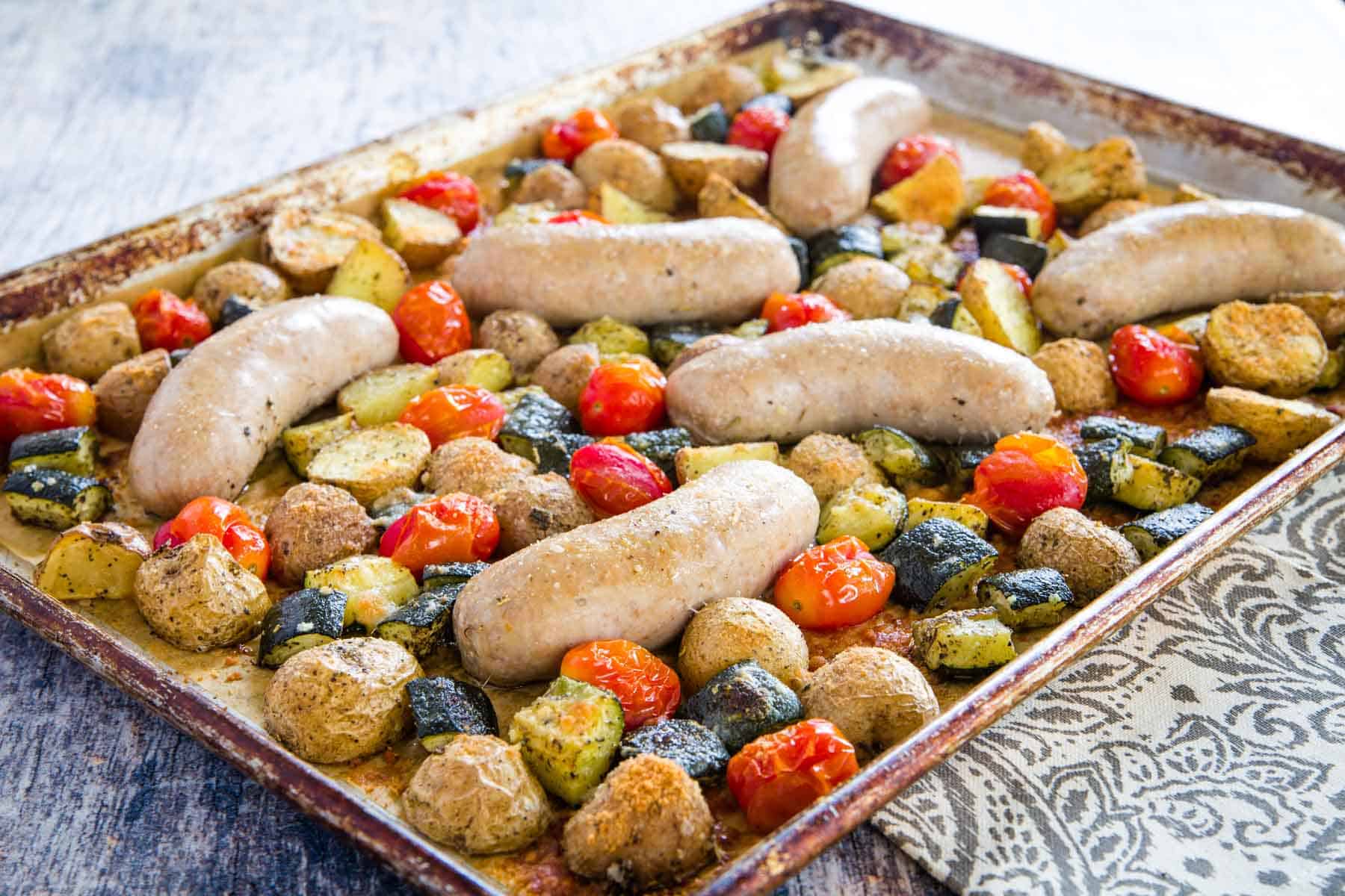 baking sheet with roasted turkey sausage, chunks of potatoes and zucchini, and grape tomatoes