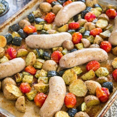 turkey sausage sheet pan dinner on the parchment-lined baking sheet with potatoes, zucchini, and tomatoes