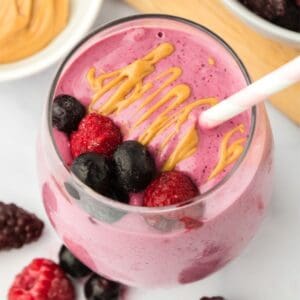 A berry smoothie in a glass topped with peanut butter and mixed berries.