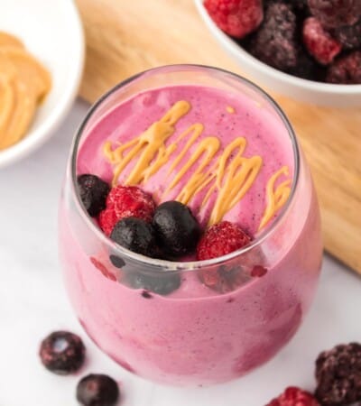 glass of a berry smoothie with a garnish of peanut butter and berries on top