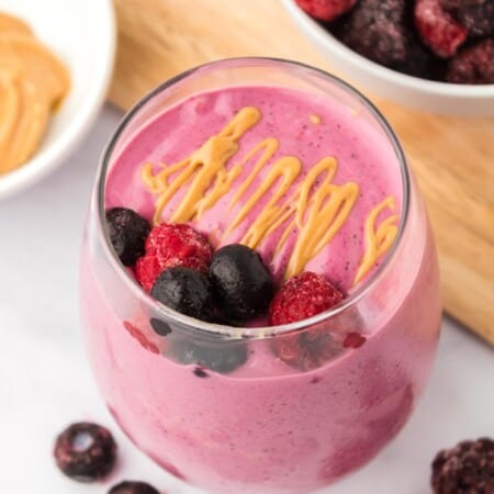 glass of a berry smoothie with a garnish of peanut butter and berries on top