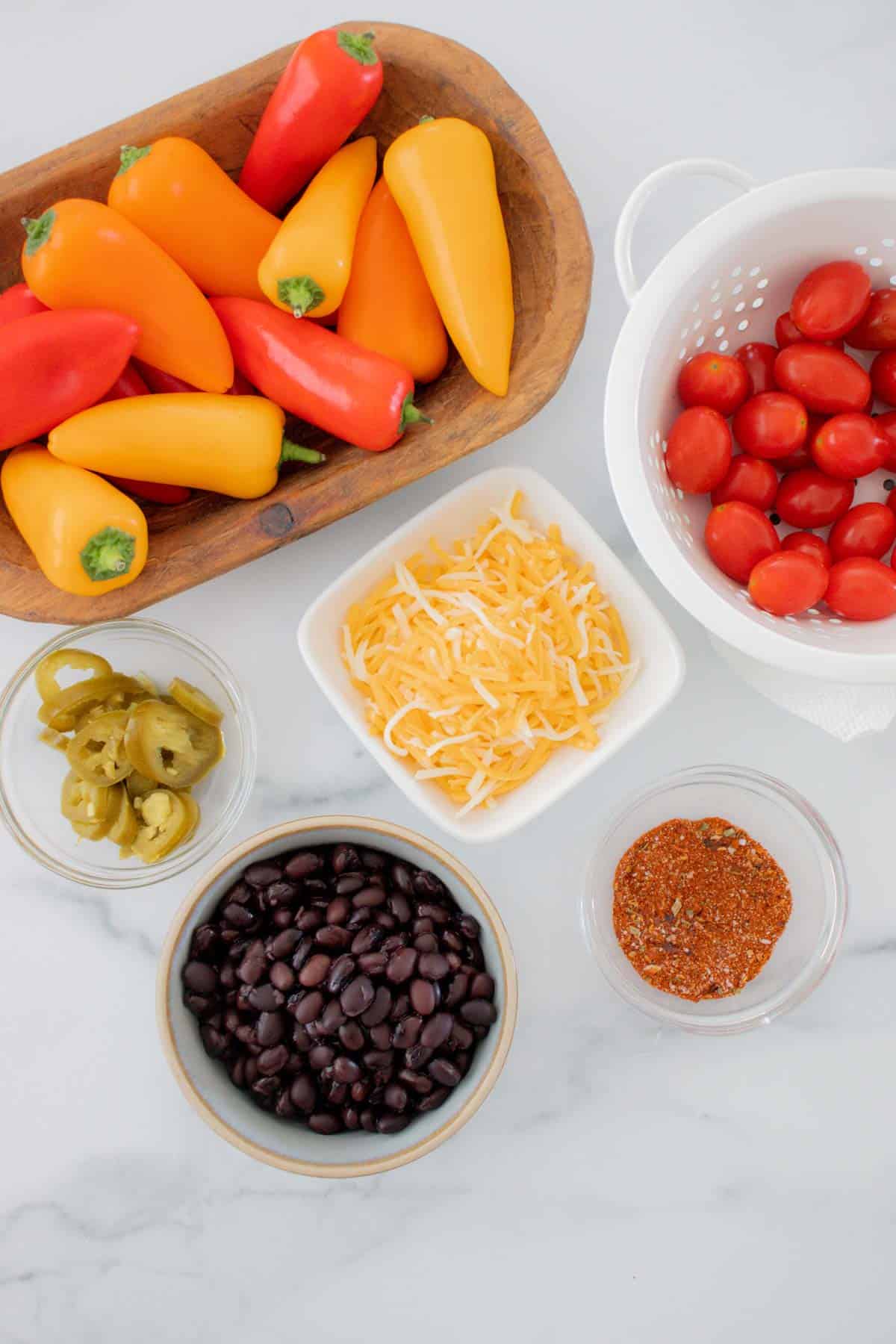 bowls of mini bell peppers, taco seasoning, black beans, grape tomatoes, jalapeno slices, and shredded cheese