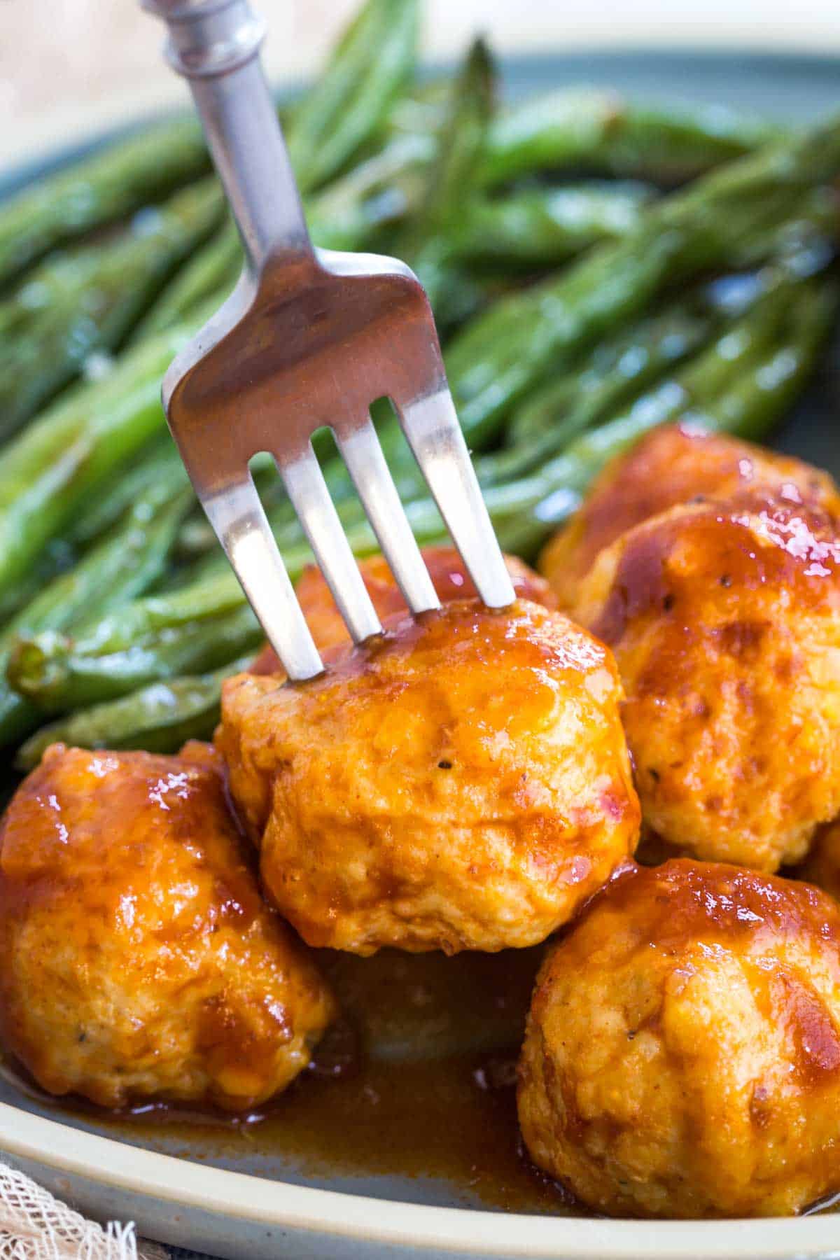 fork picking up a barbecue turkey meatball from a plate with green beans on it