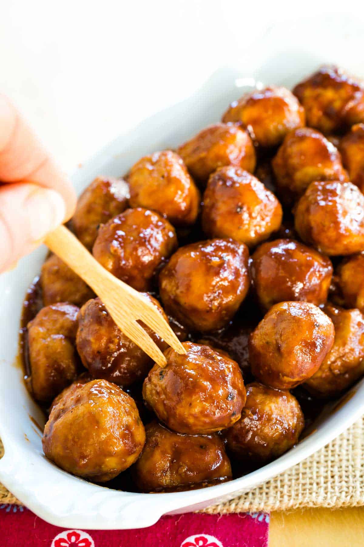 piercing a small cocktail pick into one of the barbecue turkey meatballs in a serving dish