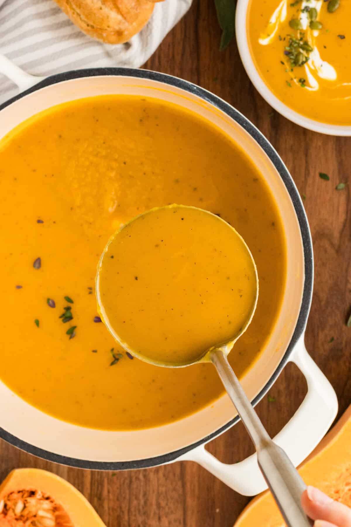 Overhead view of a ladle above a pot of butternut squash soup.