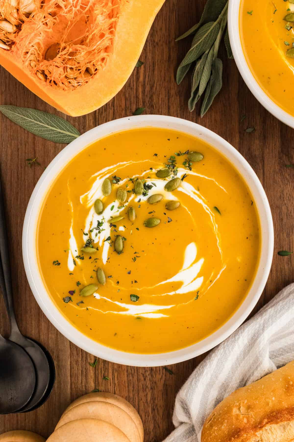 Overhead view of a bowl of butternut squash soup with cream, pepitas, and herbs ont op