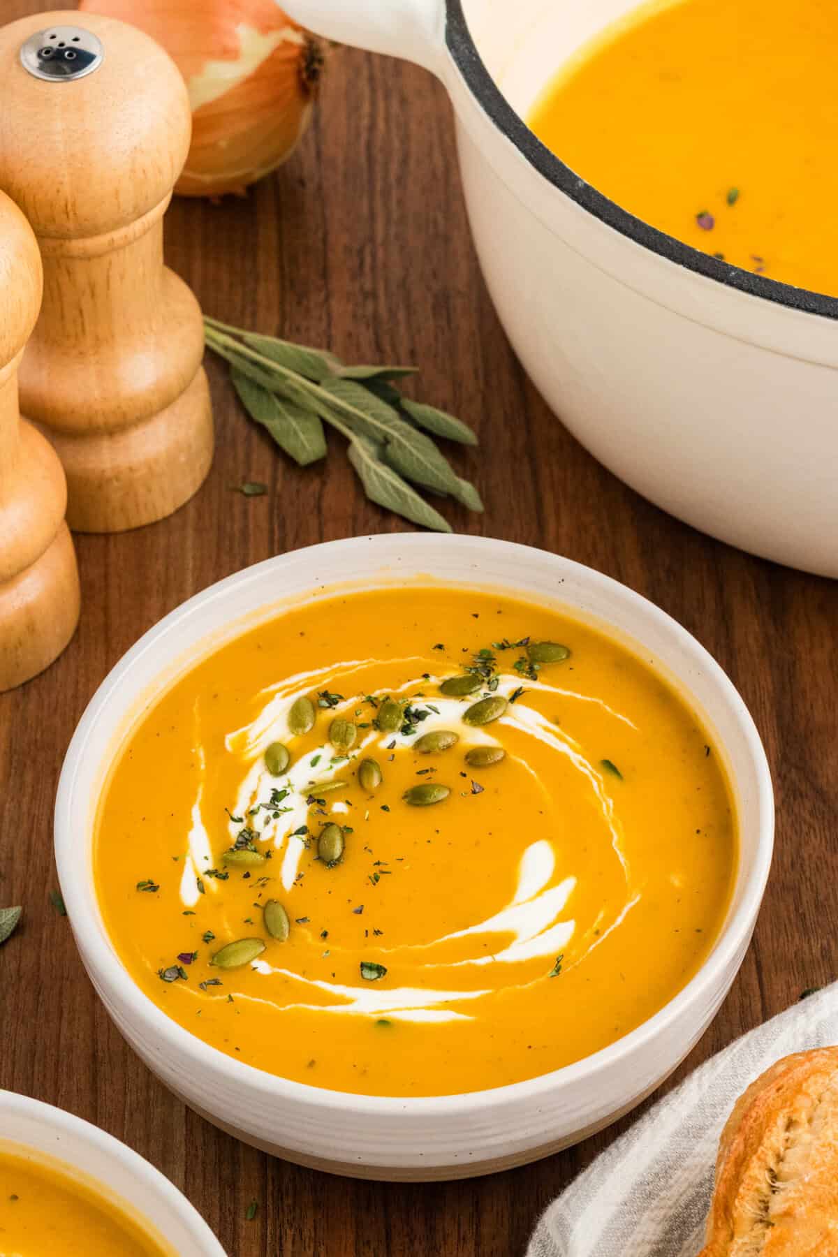A bowl of butternut squash soup next to a pot of soup.