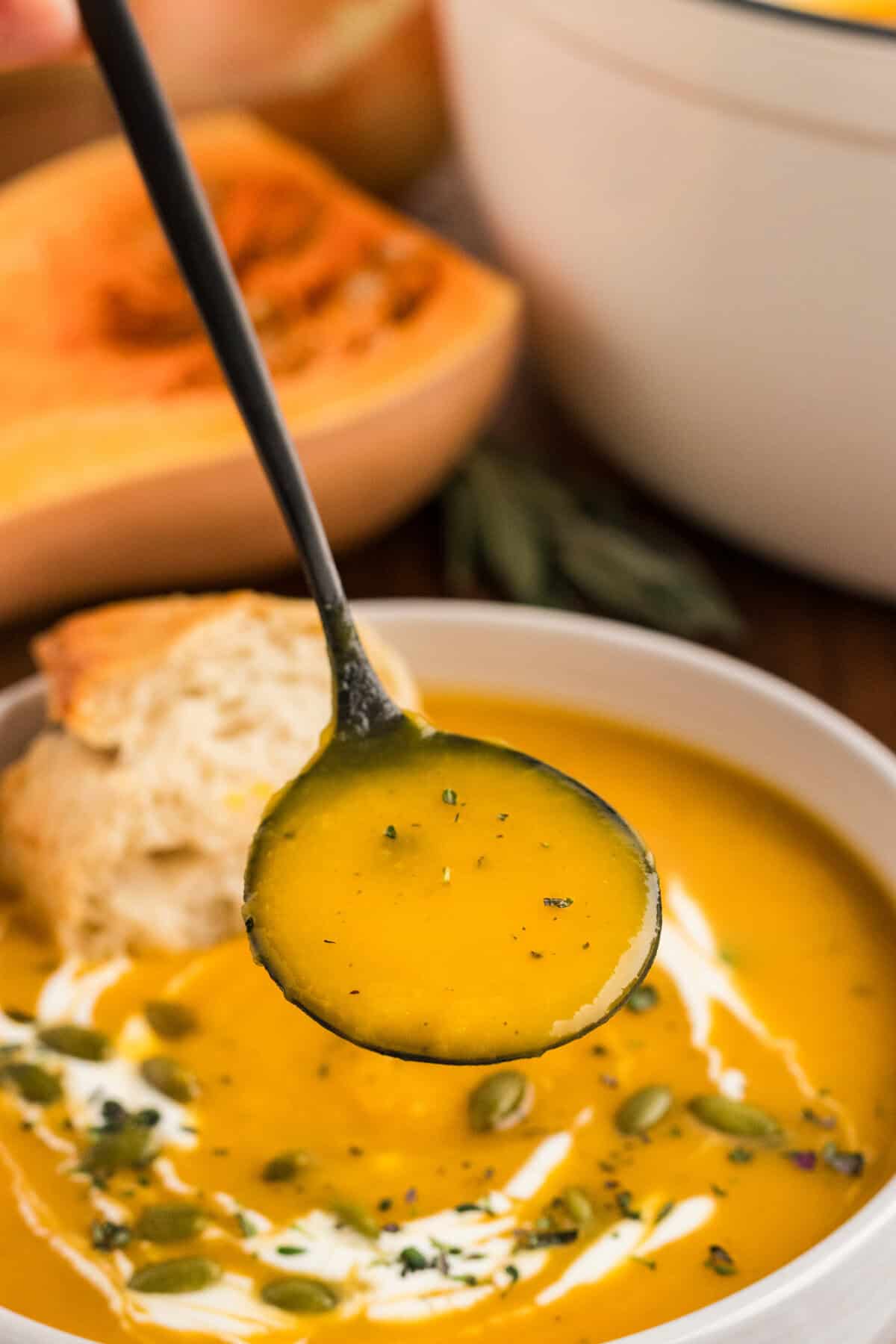 A spoon above a bowl of butternut squash soup.