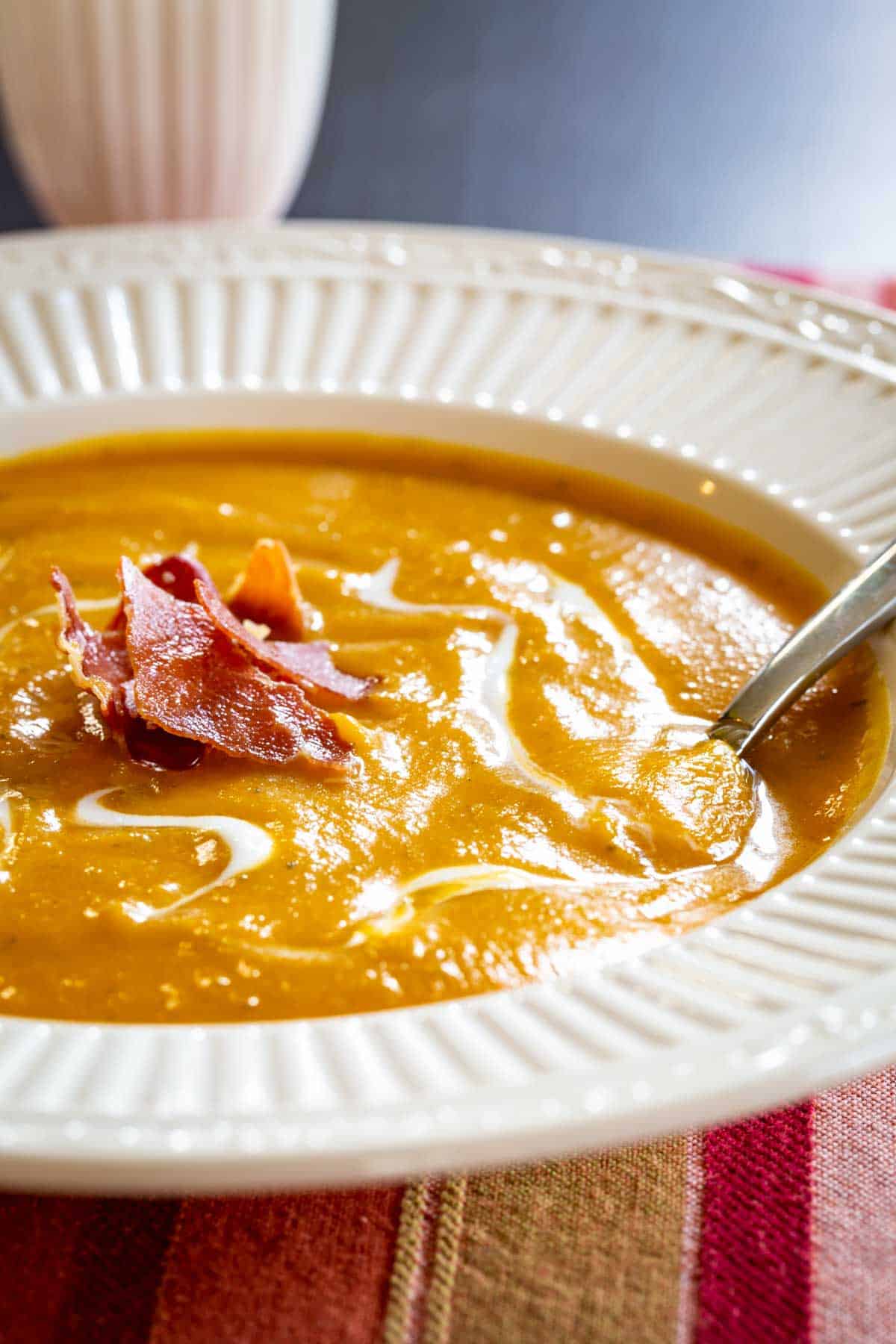 spoon set in a bowl of a creamy orange-colored pureed soup topped with crispy bits of prosciutto