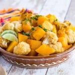 chili lime roasted cauliflower and butternut squash in a shallow terra cotta bowl on top of a colorful striped napkin with a wooden serving spoon