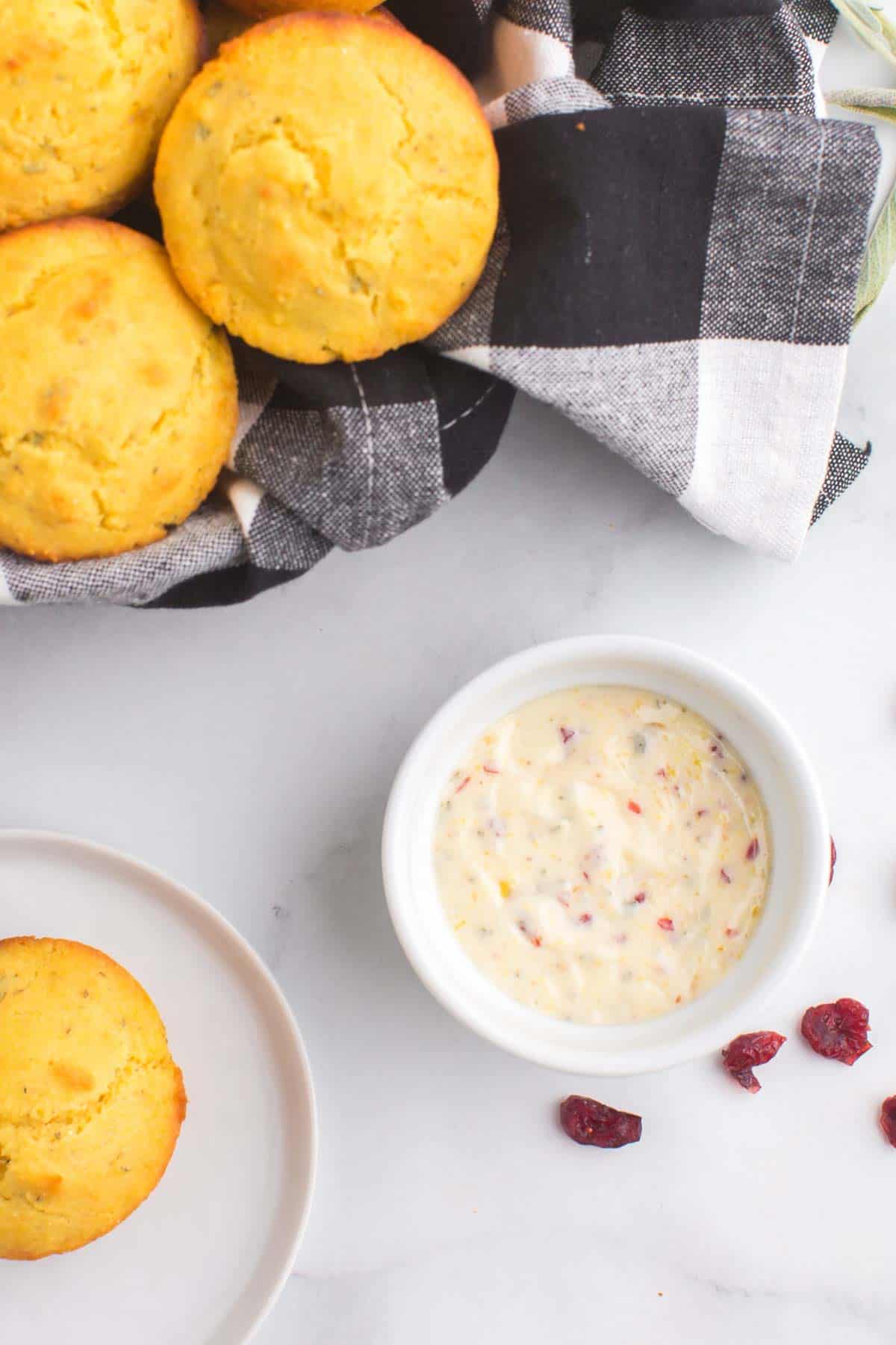 a dish of cranberry orange butter on a table with a basket of corn muffins and one on a plate