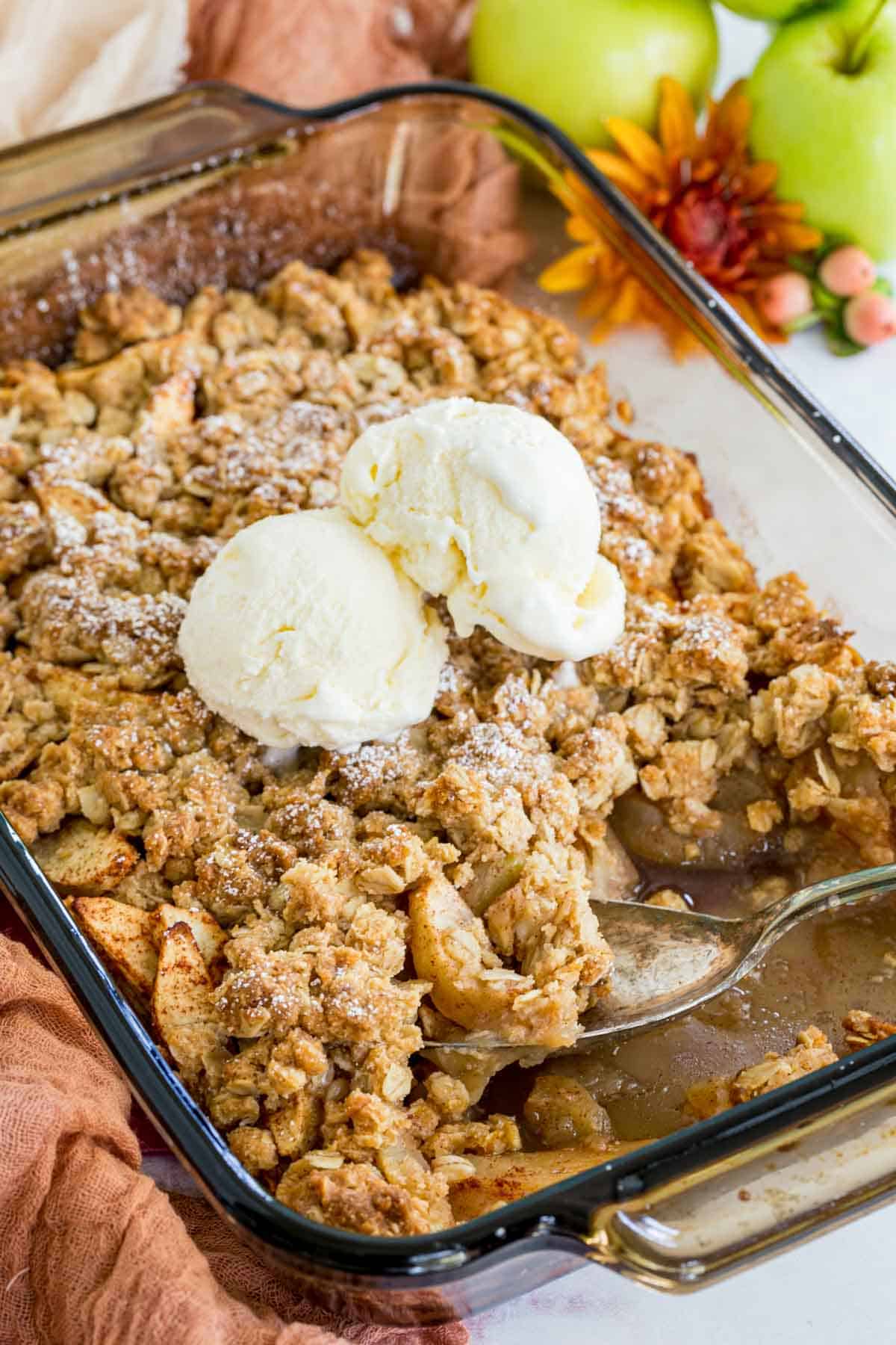 spoon in a baking dish of gluten free apple crisp topped with vanilla ice cream