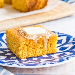 A pat of butter melting over the top of a piece of gluten free cornbread on a blue and white plate.