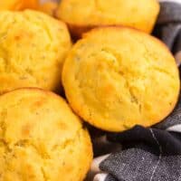 a pile of gluten free cornbread muffins in a basket lined with a black and white plaid napkin