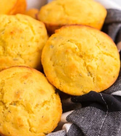a pile of gluten free cornbread muffins in a basket lined with a black and white plaid napkin