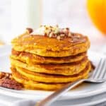 a stack of pumpkin pancakes on a plate topped with chopped pecans, butter, and syrup