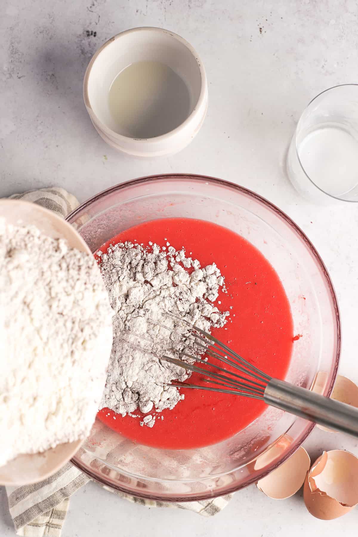 adding dry ingredients to red velvet cupcake batter in a mixing bowl