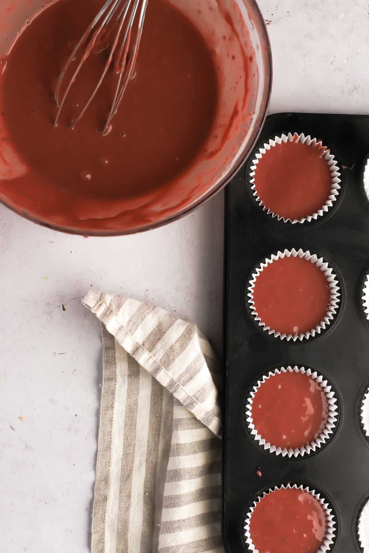 cupcake pan filled with red velvet batter and a mixing bowl of more batter