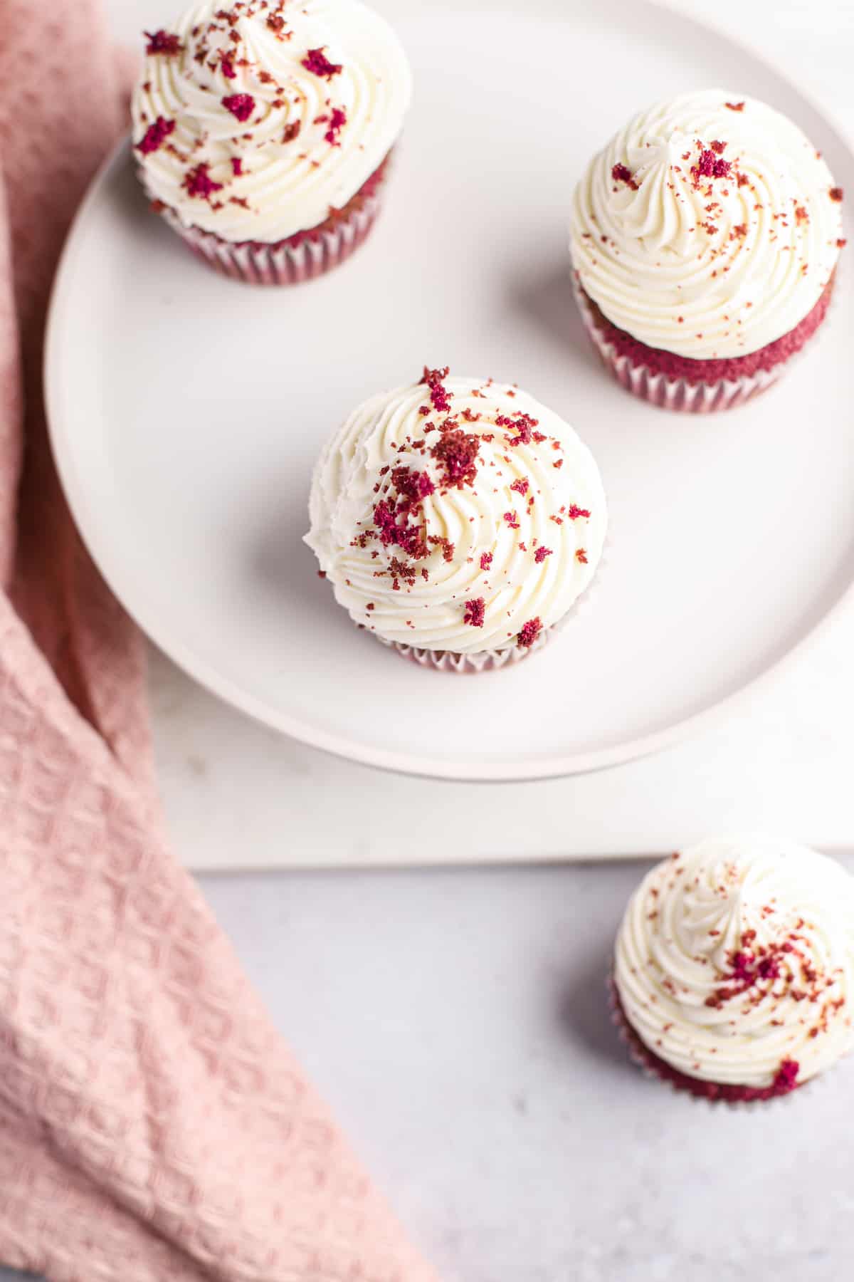 overhead of red velvet cupcakes on a cake plate with white frosting